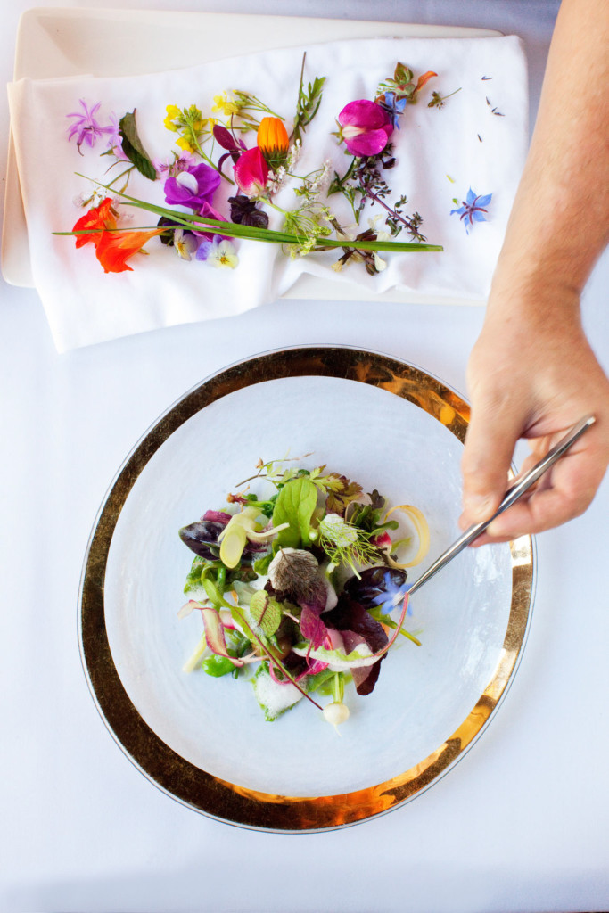A chef carefully places a garnish on a delicious mixed green salad