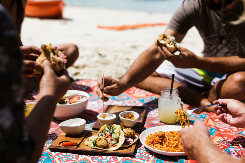 Group sitting on beach blanket enjoying a meal